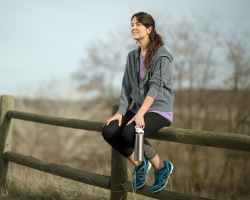 A woman sits on a wooden fence rail