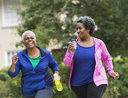 Two African American women in exercise clothes, walking down a street, holding water bottles.